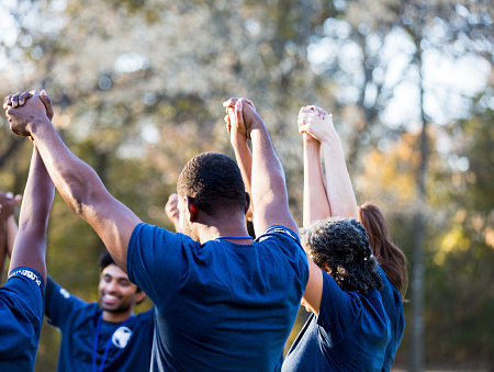 Rear view of a large group of friends and neighbors after cleaning up their neighborhood park. They are holding hands with their hands raised in unity.