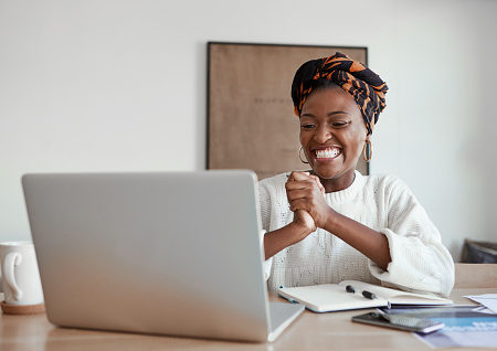 Shot of a young woman cheering while working on a laptop at home