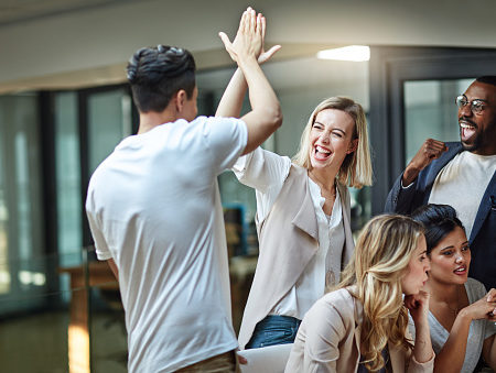 Shot of a group of colleagues giving each other a high five while using a computer together at work