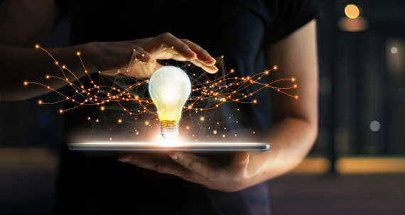 Abstract. Innovation. Hands holding tablet with light bulb future technologies and network connection on virtual interface background, innovative technology in science and communication concept.