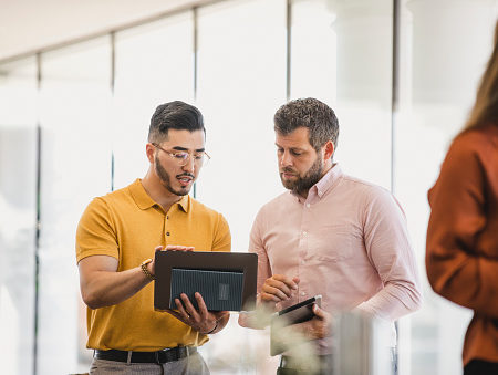 Hipster man holding laptop and explaining to coworker, support, guidance, advice