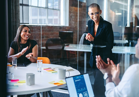 Happy young businesswoman being applauded by her colleagues during a meeting in a modern office. Successful young businesswoman smiling cheerfully while receiving praise from her colleagues.